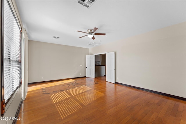 empty room with wood-type flooring, visible vents, and baseboards