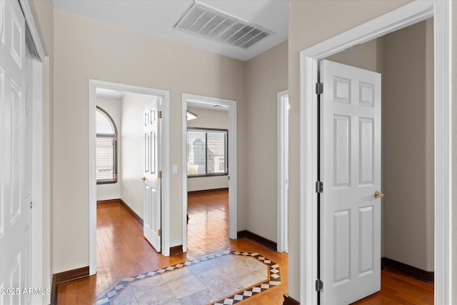 corridor with baseboards, visible vents, and hardwood / wood-style floors