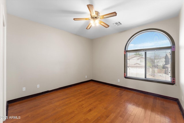 empty room featuring a ceiling fan, wood-type flooring, visible vents, and baseboards