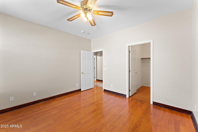 unfurnished bedroom with ceiling fan, light wood finished floors, a walk in closet, and baseboards