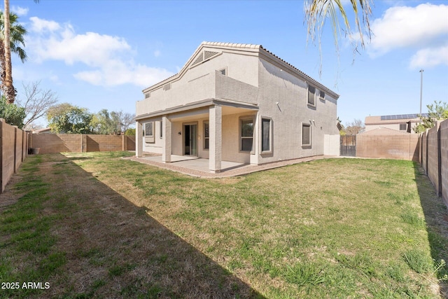 rear view of house with a fenced backyard, a tile roof, a yard, stucco siding, and a patio area