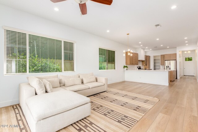 living room with a healthy amount of sunlight, ceiling fan with notable chandelier, and light hardwood / wood-style flooring