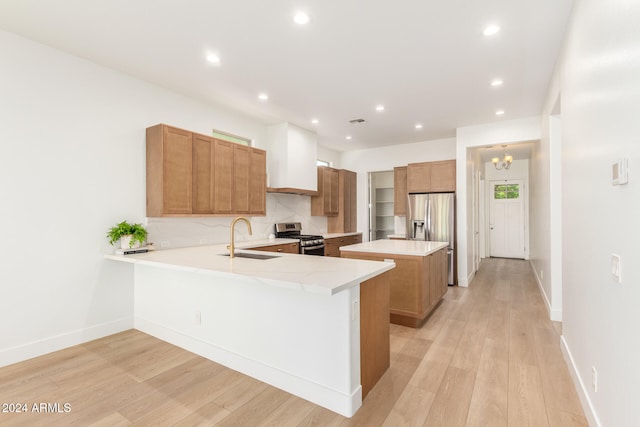 kitchen with sink, kitchen peninsula, appliances with stainless steel finishes, a notable chandelier, and light hardwood / wood-style floors