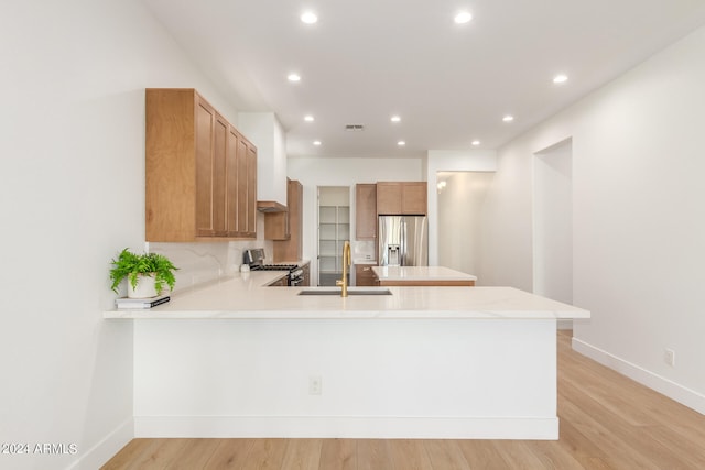 kitchen featuring appliances with stainless steel finishes, decorative backsplash, light hardwood / wood-style floors, kitchen peninsula, and sink