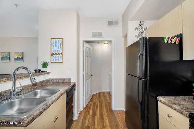 kitchen with a sink, light brown cabinets, light wood-style flooring, visible vents, and black appliances
