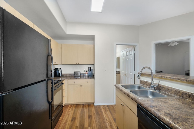 kitchen with a sink, light wood-style flooring, black appliances, and dark countertops