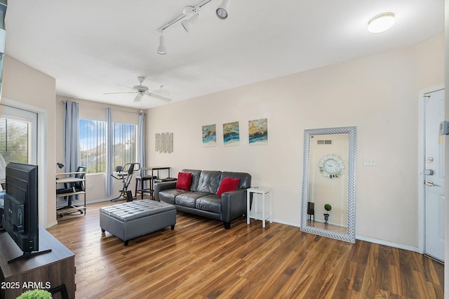 living area with track lighting, a wood stove, wood finished floors, baseboards, and ceiling fan
