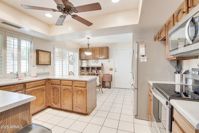 kitchen featuring pendant lighting, light tile patterned floors, stainless steel appliances, a raised ceiling, and kitchen peninsula