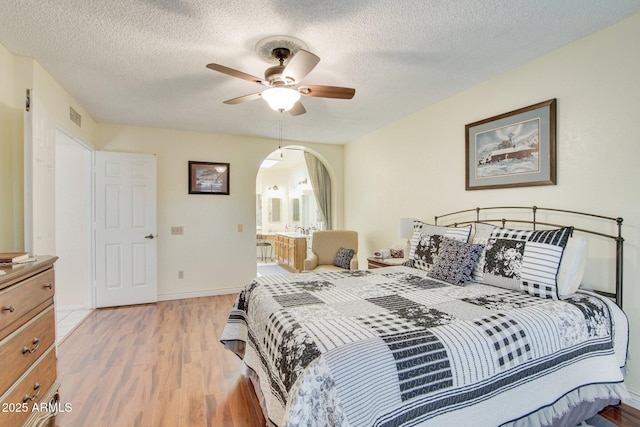 bedroom with a textured ceiling, light hardwood / wood-style flooring, ensuite bath, and ceiling fan