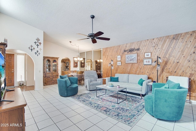 tiled living room with lofted ceiling, ceiling fan with notable chandelier, a textured ceiling, and wood walls