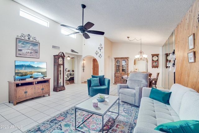 tiled living room with ceiling fan with notable chandelier, high vaulted ceiling, a textured ceiling, and wood walls