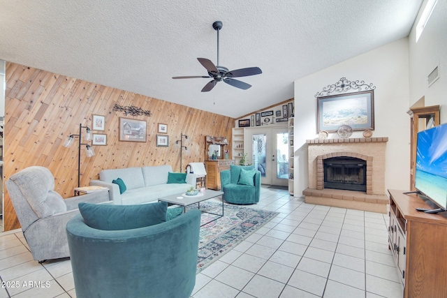 tiled living room with wood walls, lofted ceiling, ceiling fan, a textured ceiling, and french doors