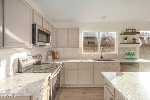 kitchen featuring sink, light stone countertops, appliances with stainless steel finishes, tasteful backsplash, and light hardwood / wood-style floors