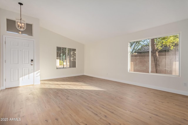 unfurnished living room featuring vaulted ceiling, an inviting chandelier, and light hardwood / wood-style flooring