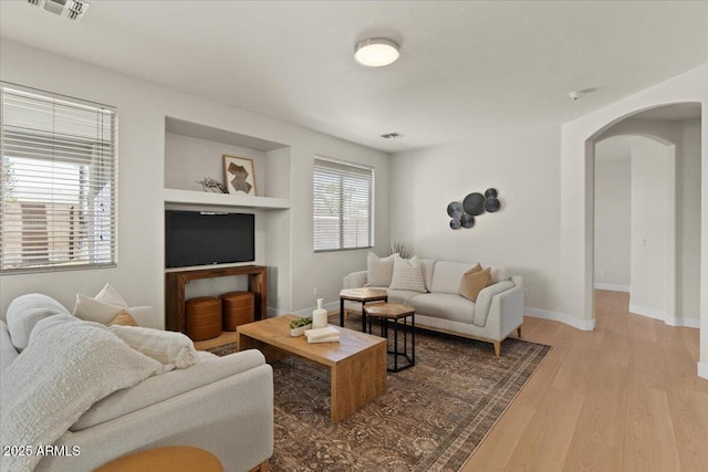 living area with arched walkways, built in features, baseboards, wood finished floors, and visible vents