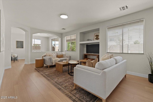 living room with visible vents, arched walkways, light wood finished floors, and built in shelves