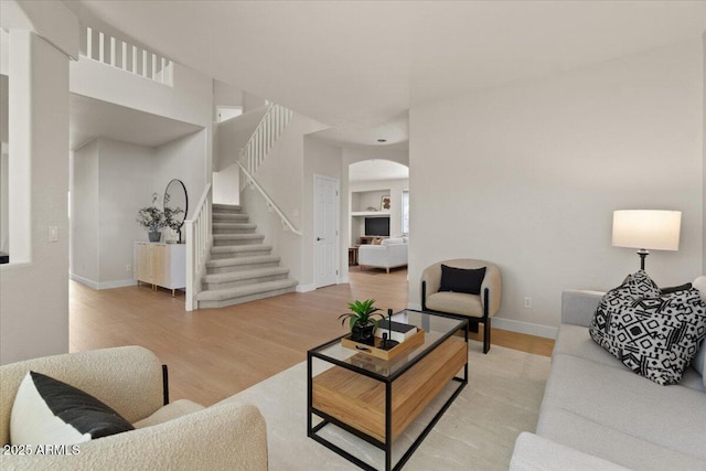 living room featuring arched walkways, baseboards, light wood finished floors, and stairway