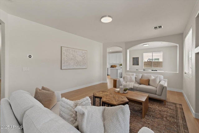 living room with light wood-style floors, arched walkways, baseboards, and visible vents