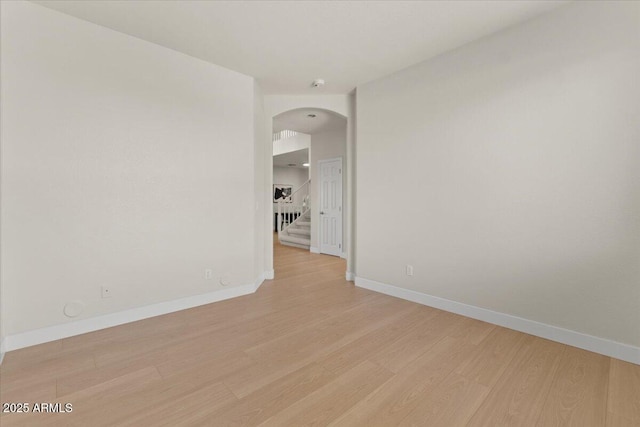 spare room featuring arched walkways, baseboards, and light wood-type flooring