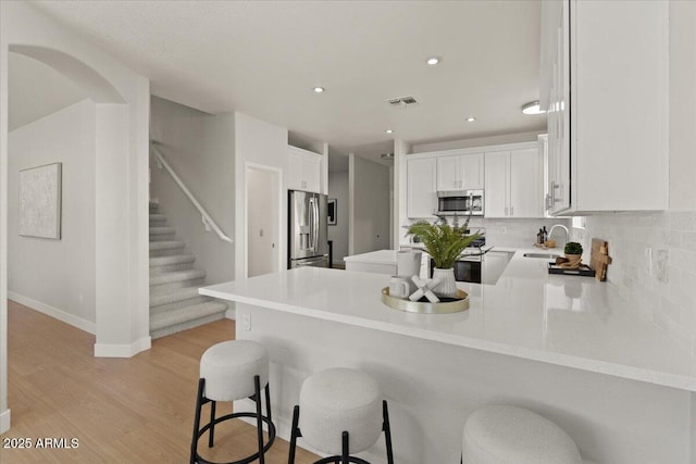 kitchen featuring appliances with stainless steel finishes, a sink, a peninsula, decorative backsplash, and light wood-type flooring