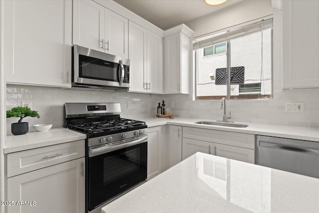 kitchen featuring appliances with stainless steel finishes, tasteful backsplash, a sink, light stone counters, and white cabinets