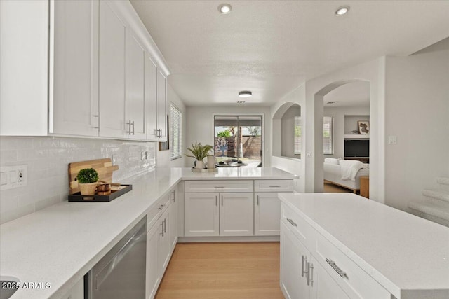 kitchen with stainless steel dishwasher, white cabinetry, decorative backsplash, and light countertops
