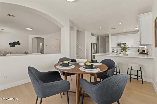 dining area with visible vents, arched walkways, baseboards, stairs, and light wood-style flooring