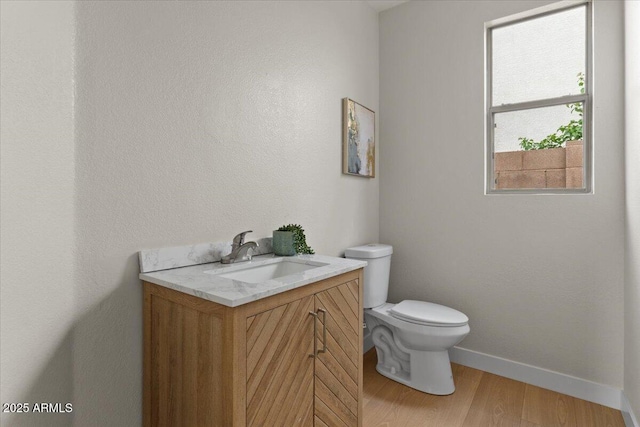 half bath with baseboards, vanity, toilet, and wood finished floors
