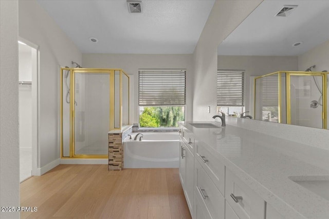 full bath with a bath, visible vents, a shower stall, wood finished floors, and a sink