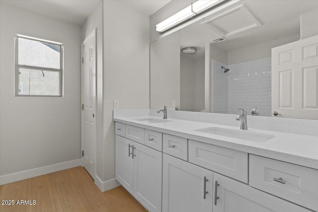 bathroom with a sink, double vanity, a tile shower, and wood finished floors