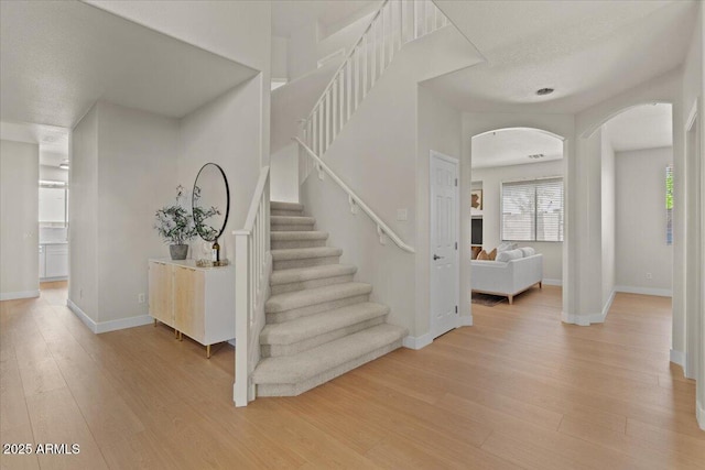 stairs with arched walkways, baseboards, and wood finished floors