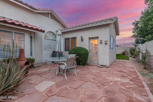 patio terrace at dusk with outdoor dining space and a fenced backyard