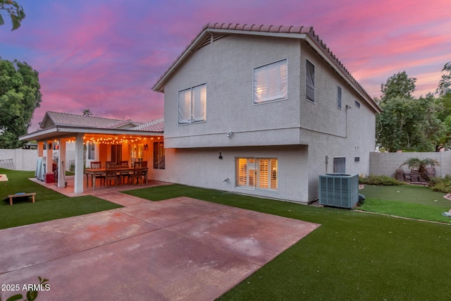 back of house at dusk featuring a patio area, a yard, central AC, and fence