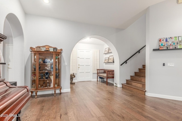 interior space featuring baseboards, arched walkways, wood finished floors, and stairs