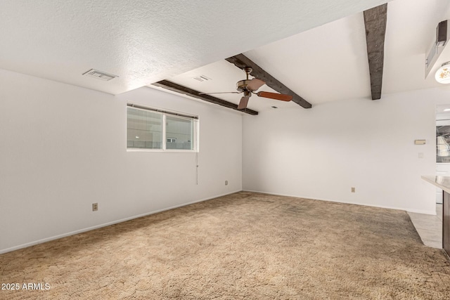 unfurnished room with visible vents, ceiling fan, beamed ceiling, a textured ceiling, and carpet floors