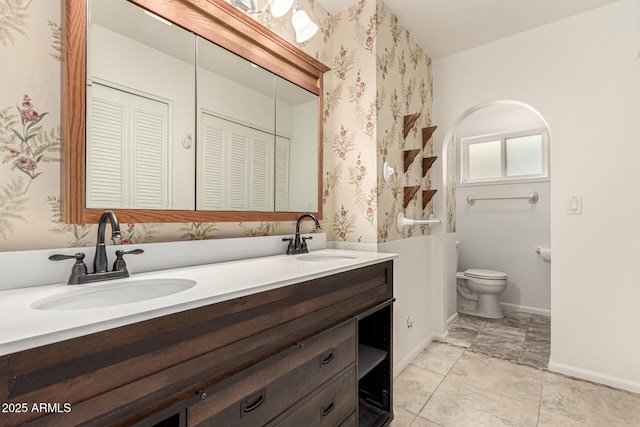 full bathroom featuring double vanity, a sink, toilet, and baseboards