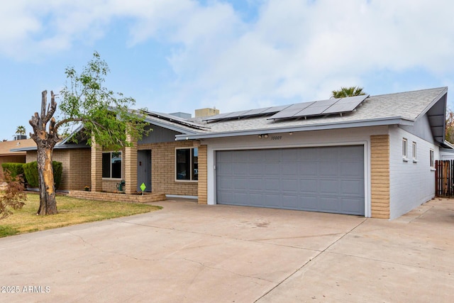 view of front of home with a garage, concrete driveway, brick siding, and solar panels