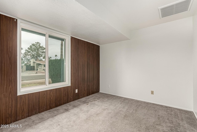 empty room with carpet, visible vents, and wooden walls