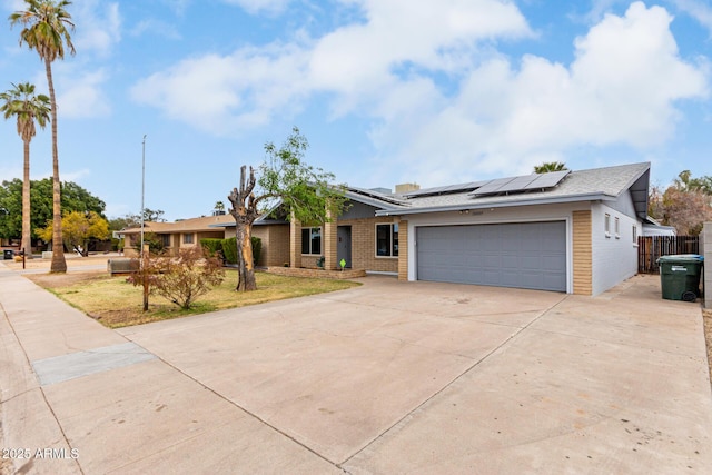 mid-century home with a garage, solar panels, concrete driveway, fence, and brick siding