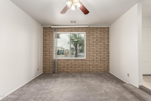 unfurnished room featuring visible vents, carpet flooring, ceiling fan, brick wall, and baseboards