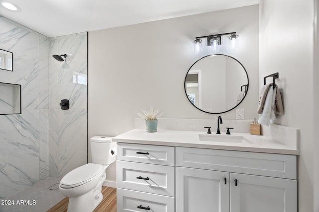 bathroom with vanity, toilet, a tile shower, and wood-type flooring