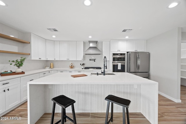 kitchen with white cabinetry, sink, stainless steel appliances, an island with sink, and custom range hood