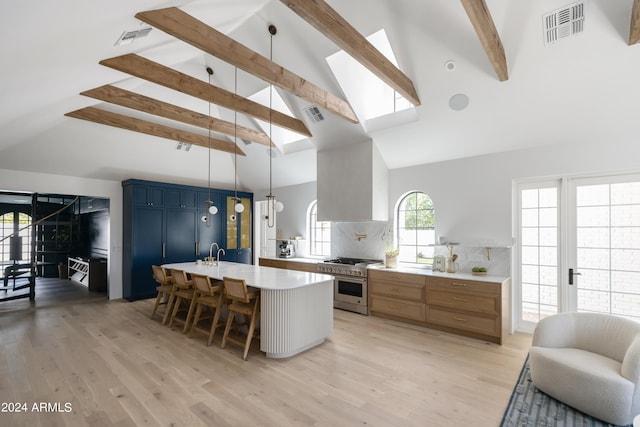 kitchen with decorative backsplash, decorative light fixtures, range with two ovens, a center island with sink, and a breakfast bar area