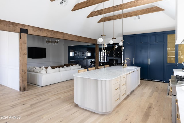 kitchen with beam ceiling, hanging light fixtures, blue cabinets, a kitchen island with sink, and white cabinets