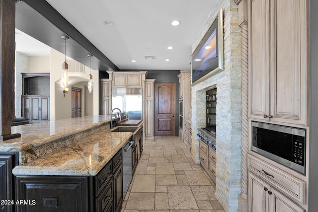 kitchen featuring light stone countertops, a large island with sink, built in appliances, decorative light fixtures, and cream cabinets