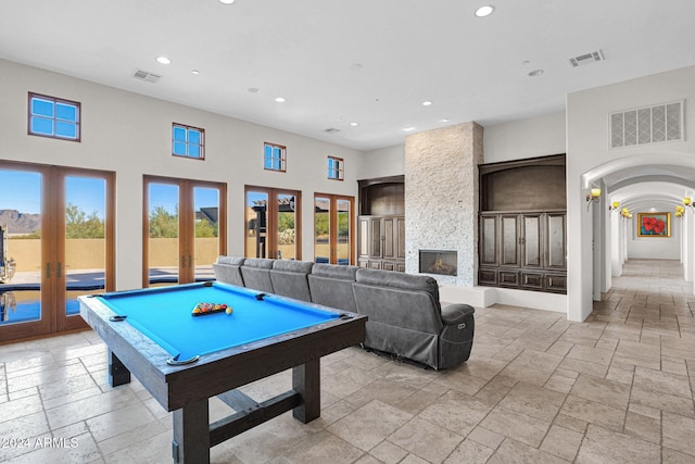 playroom featuring a stone fireplace, a towering ceiling, pool table, and french doors