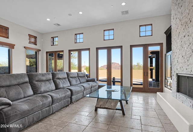 living room with a fireplace, plenty of natural light, a towering ceiling, and french doors