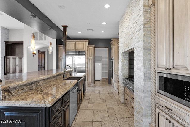 kitchen with built in appliances, light stone countertops, sink, and hanging light fixtures