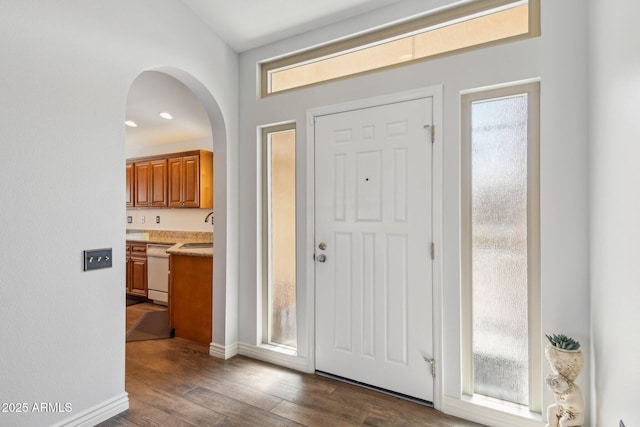 foyer featuring dark wood-style floors, arched walkways, and baseboards