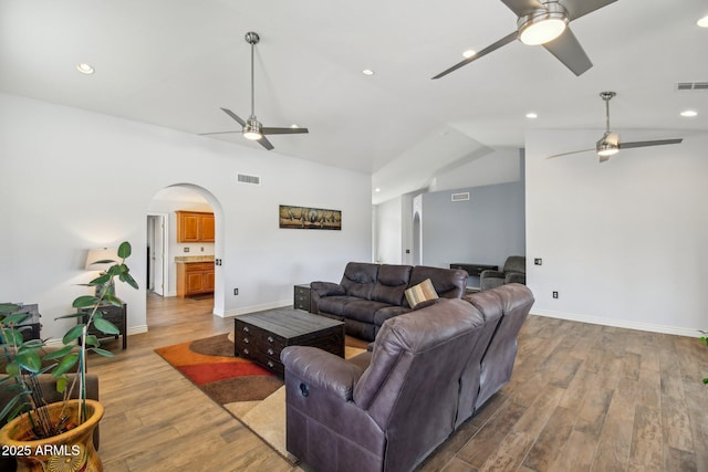 living room featuring light wood-style floors, ceiling fan, visible vents, and arched walkways